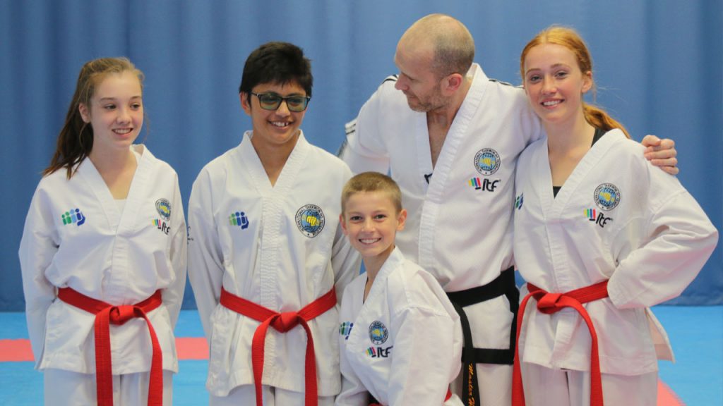 Red belt students training with Master Hutton in ITF Taekwon-Do, preparing for a turning kick session.