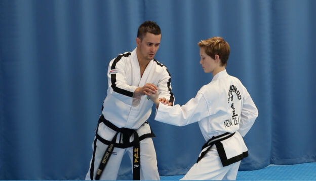 ITF Taekwon-Do instructor correcting an inner forearm block during Chon-Ji pattern practice.