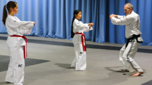 Master Hutton coaching Helen Khiev and Layla Allen on ITF Taekwon-Do pattern movements, focusing on letting go to generate speed and power
