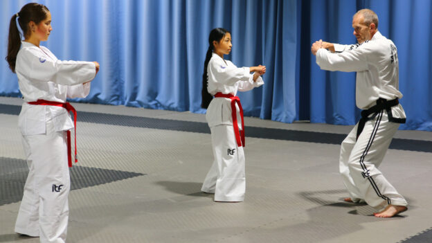 Master Hutton coaching Helen Khiev and Layla Allen on ITF Taekwon-Do pattern movements, focusing on letting go to generate speed and power