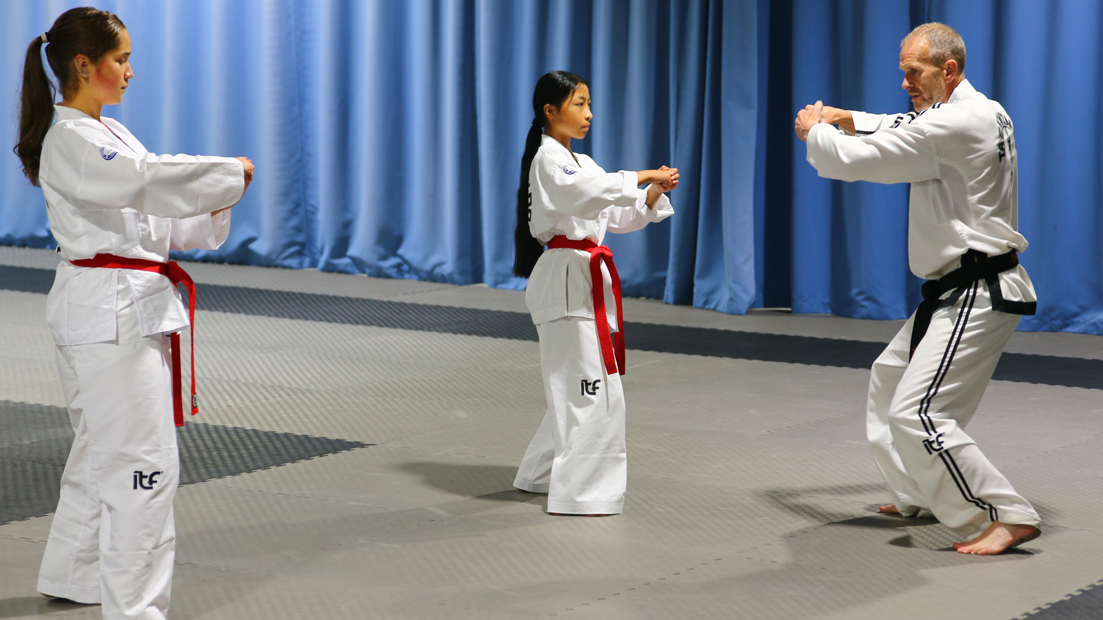 Master Hutton coaching Helen Khiev and Layla Allen on ITF Taekwon-Do pattern movements, focusing on letting go to generate speed and power