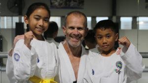 Master Mark Hutton with two young ITF Taekwon-Do students during a kids training session, demonstrating confidence and strong guard position.